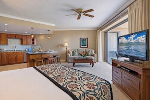 A hotel room with a bed, a TV, a dining area, a ceiling fan, and a large window.