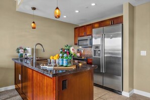 A kitchen with a central island, stainless steel appliances, wooden cabinets, and pendant lighting.