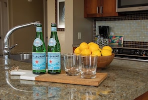 A kitchen counter with Pellegrino mineral water bottles, a bowl of lemons, and three glasses.