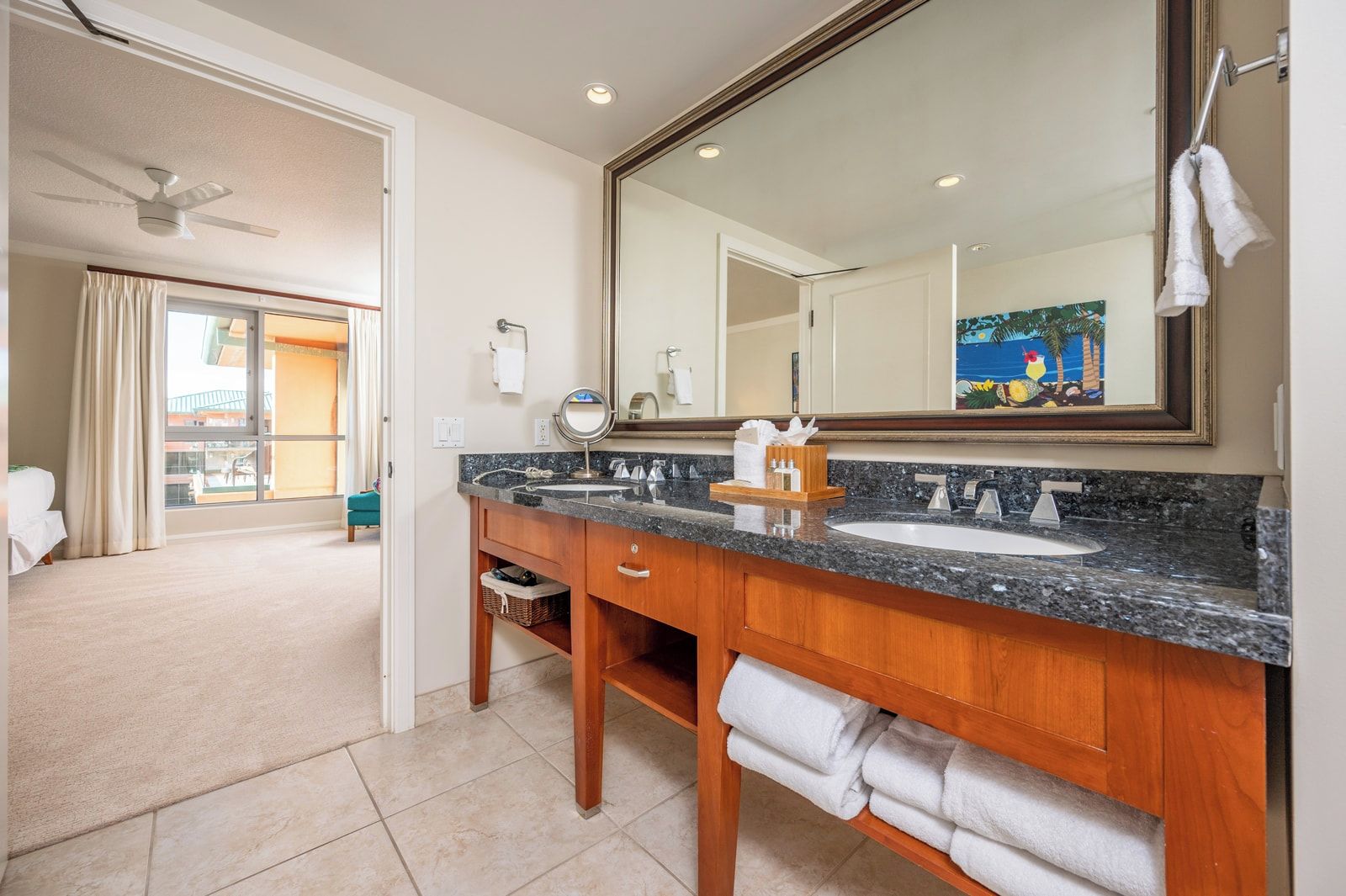 A hotel bathroom with a large mirror, two sinks, a wooden vanity, and a view of the outside.