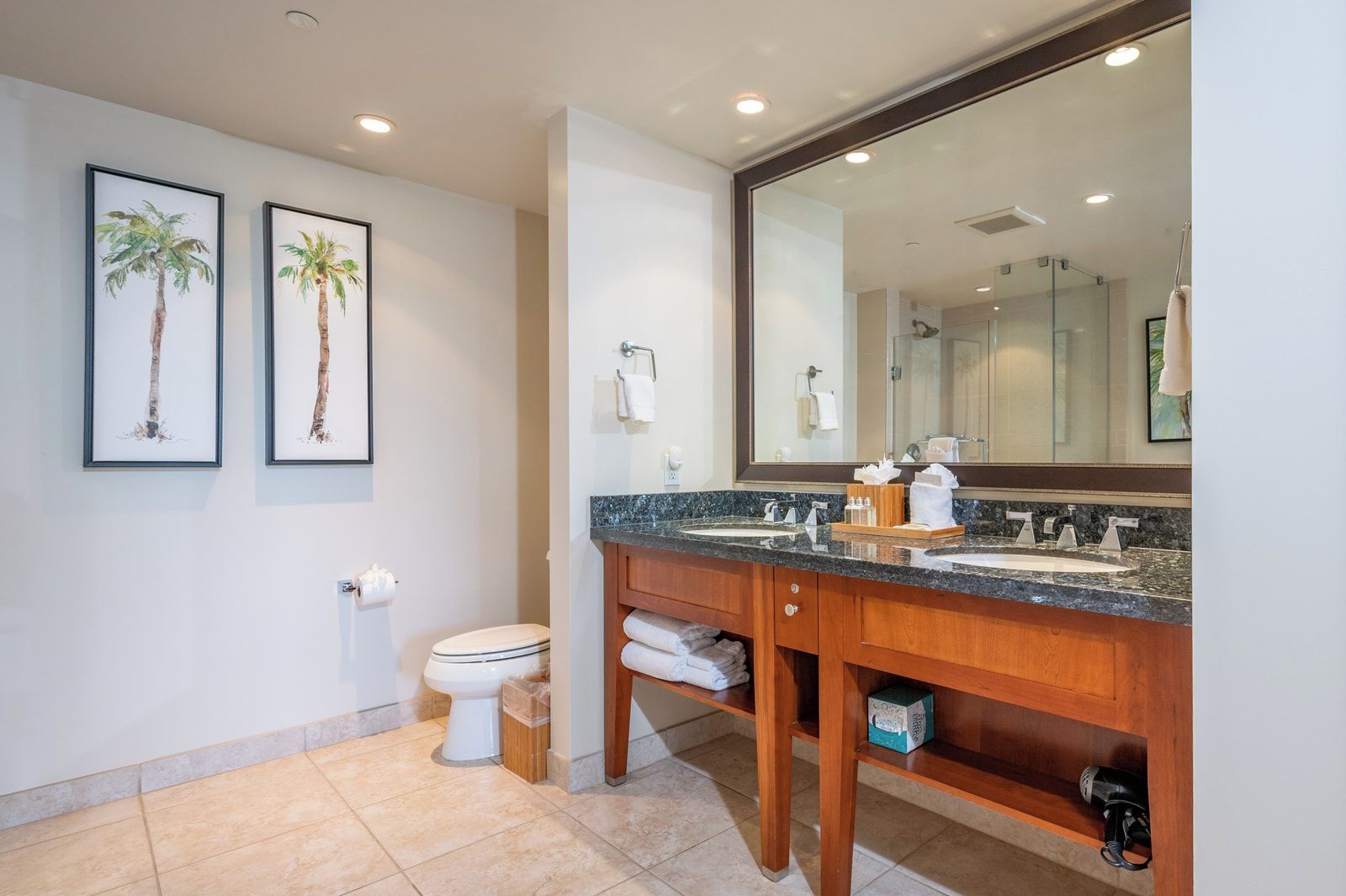 Une salle de bain avec des toilettes, un lavabo et un grand miroir. Des tableaux encadrés ornent le mur.