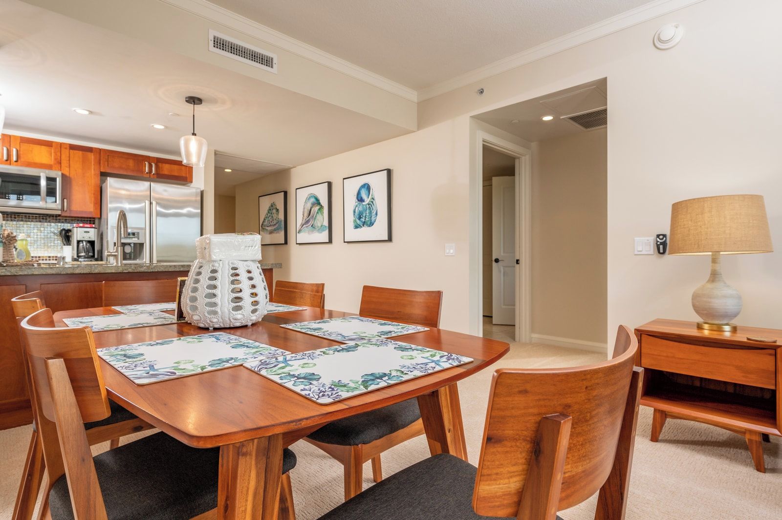 A dining area with a wooden table, chairs, a white decorative vase, and framed artwork on the wall.