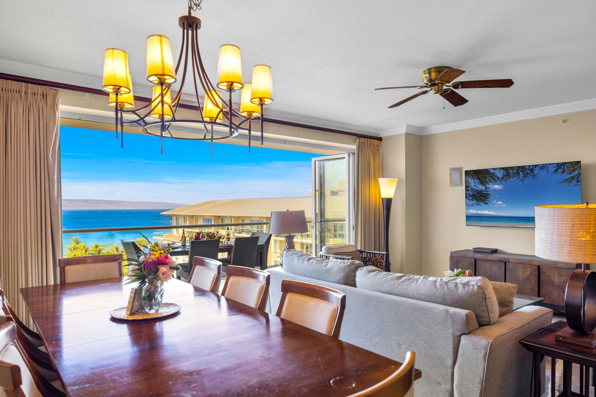A hotel room with a dining area, a sofa, a TV, and a view of the ocean.