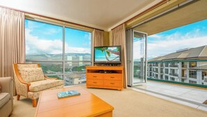 A hotel room with a large window, a television, a sofa, and a wooden coffee table.