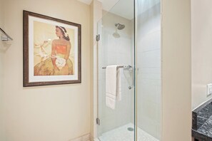 Eine begehbare, gläserne Dusche mit Handtuchhalter, ein gerahmtes Kunstwerk an der Wand und eine Marmorarbeitsplatte.