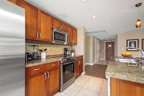 A modern kitchen with wooden cabinets, stainless steel appliances, and a granite countertop. - Honua Kai | Ocean View 4 BR, Sleeps 12 | Car Incl. w/ 6+ Nights | HKH ML-1323 by KBM (Lahaina)
