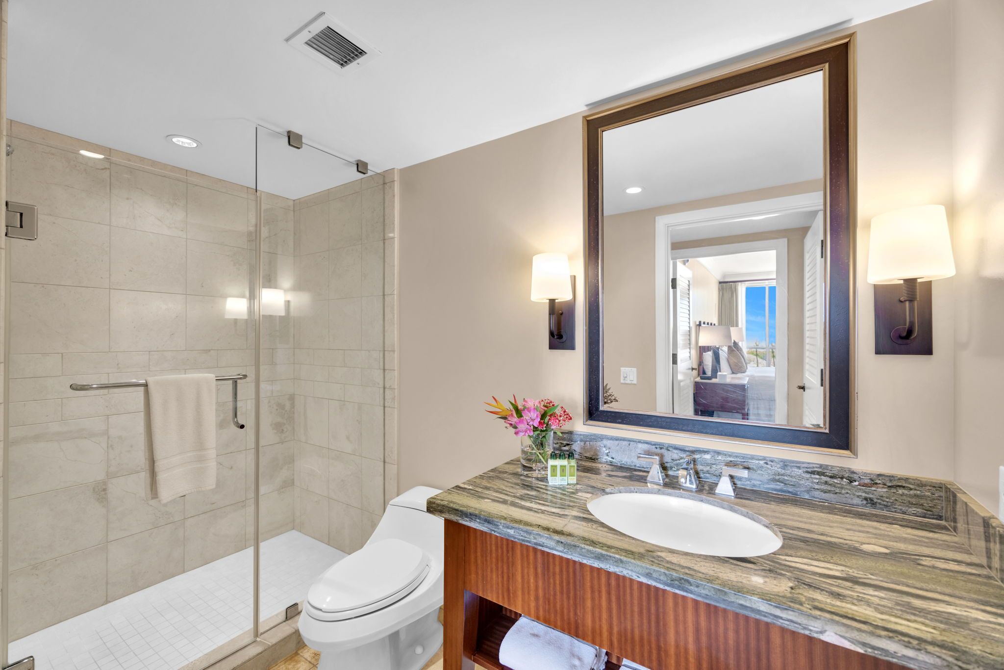 A modern bathroom with a glass shower enclosure, a white toilet, a marble sink, and a large mirror.
