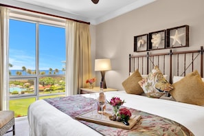 Une chambre d’hôtel avec un lit, un plateau avec une bouteille et des verres, une table de chevet avec une lampe, et une vue sur un complexe hôtelier.