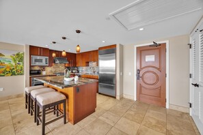 Une cuisine moderne dotée d’un îlot central, d’appareils électroménagers en acier inoxydable, de meubles de rangement en bois et d’une porte décorative.
