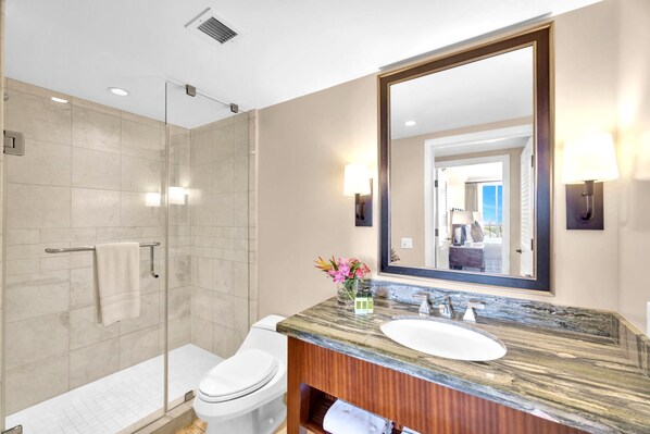 Un baño moderno con cabina de ducha de vidrio, inodoro blanco, lavabo de mármol y un espejo grande.