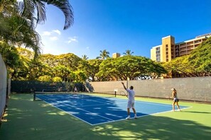 An outdoor tennis court surrounded by trees and buildings.