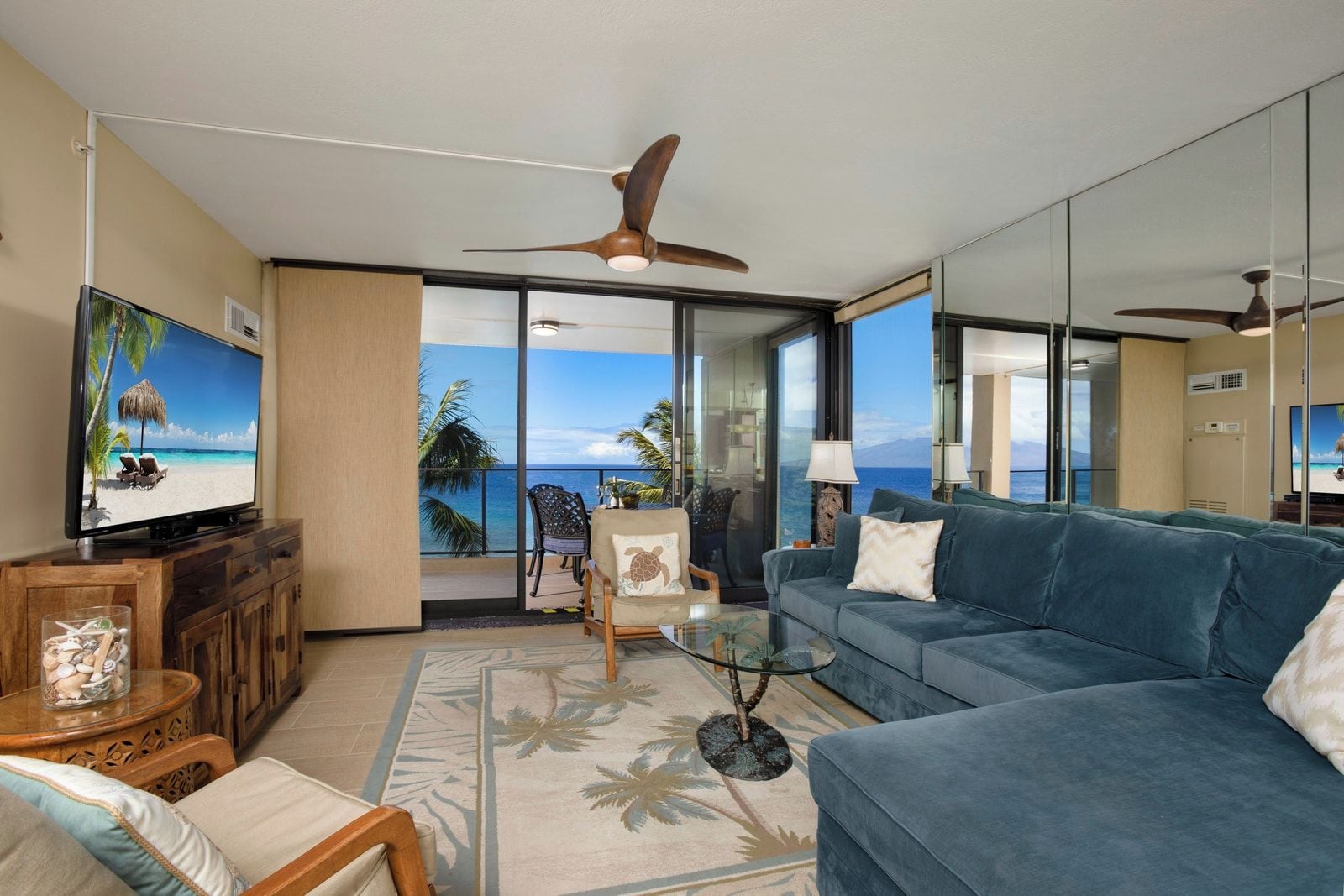 A room with a large window, a ceiling fan, a television, a sofa, and a small table with decorative items.