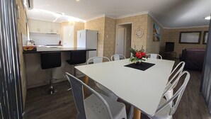 A compact kitchen with white cabinets, a white refrigerator, and a dining area with a white table and chairs. - Esperance Break Away (Esperance)