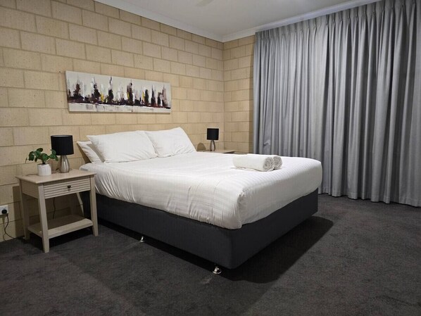 A modern bedroom with a bed, nightstands, a lamp, and a painting on the wall.