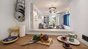 A kitchen with a view to a dining area, a cutting board with vegetables, a coffee maker, and a scale. - Sea Breeze Garavan Apt Villa New York, Menton, France (Menton)