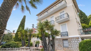 A multi-story building with balconies, surrounded by palm trees and other greenery. - Sea Breeze Garavan Apt Villa New York, Menton, France (Menton)