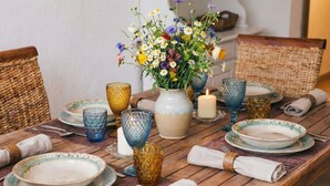 A wooden dining table set with plates, glasses, and a vase of flowers.