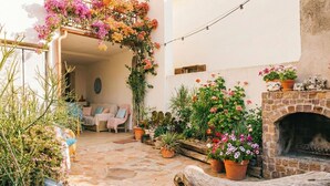 An outdoor patio with a stone floor, a wooden bench, and various potted plants and flowers.