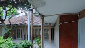 A covered outdoor area with a tiled floor, a red brick wall, and a tree. - Griya Al Mukmin (Surakarta)