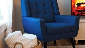 Een blauwe fauteuil, een rieten mand met handdoeken en een vloerkleed in een kamer met een open haard.