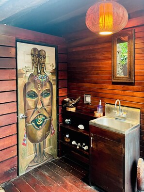 A wooden interior with a door featuring a painted face, a sink, shelves with various items, and a hanging light fixture. - Miami Tiny House • Urban Glamping Solo Micro Space in Posh Coconut Grove (Miami)