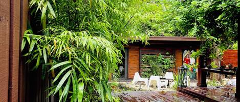 A wooden deck with a garden area, including bamboo plants and a small structure with chairs.
