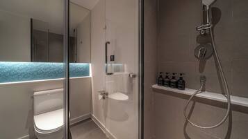 A modern bathroom with a glass-enclosed shower, a toilet, and a shelf with toiletries.