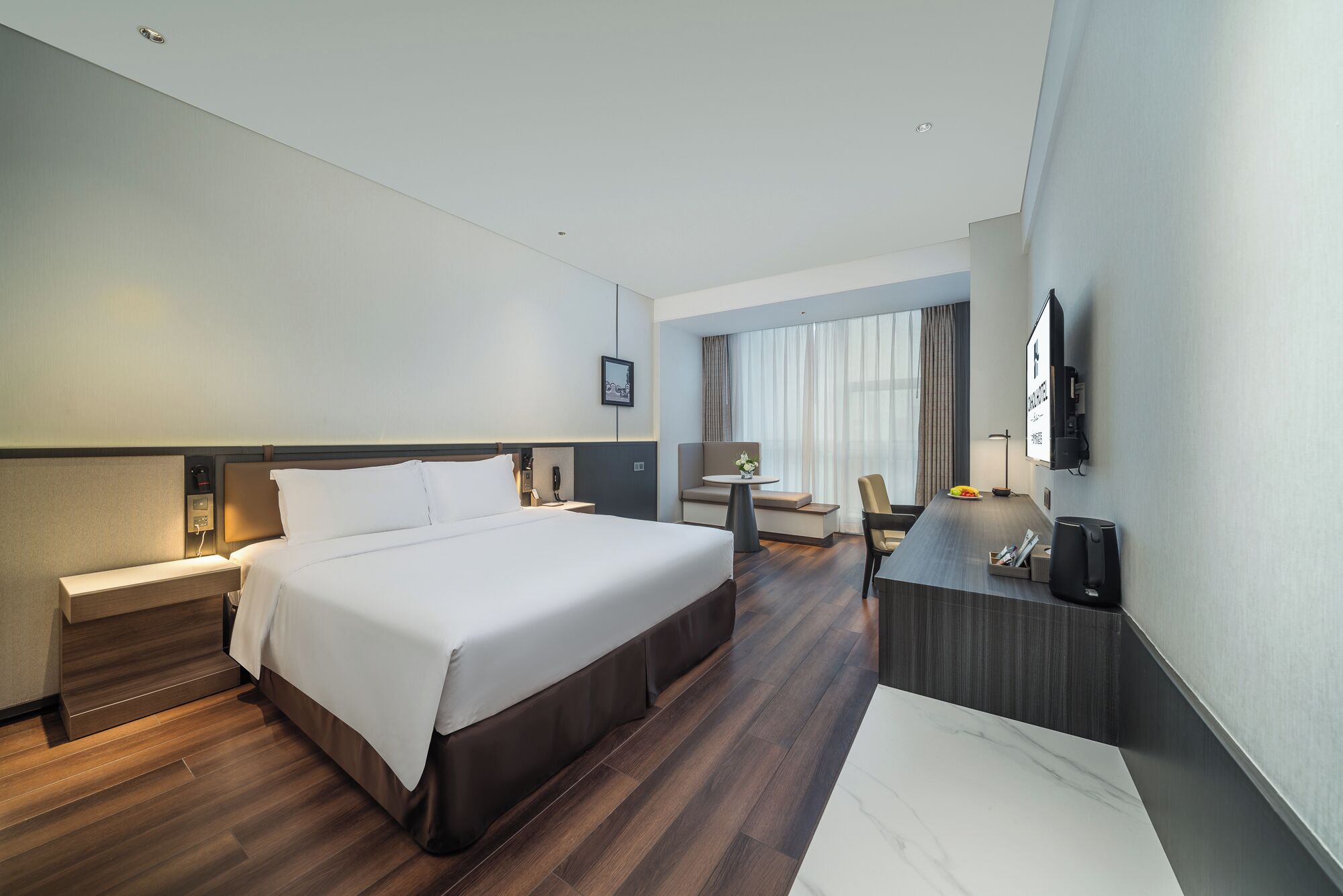 A hotel room with a large bed, a desk, a chair, a TV, and a window with curtains.