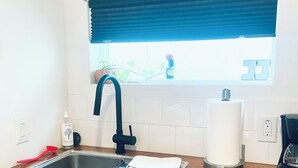 A kitchen with a stainless steel sink, a black faucet, a white towel on the counter, a coffee maker, and a window with blue blinds. - ‘Señorita Sunset’ Guest Fave! Chic Studio Montrose Walkable area! (Houston)