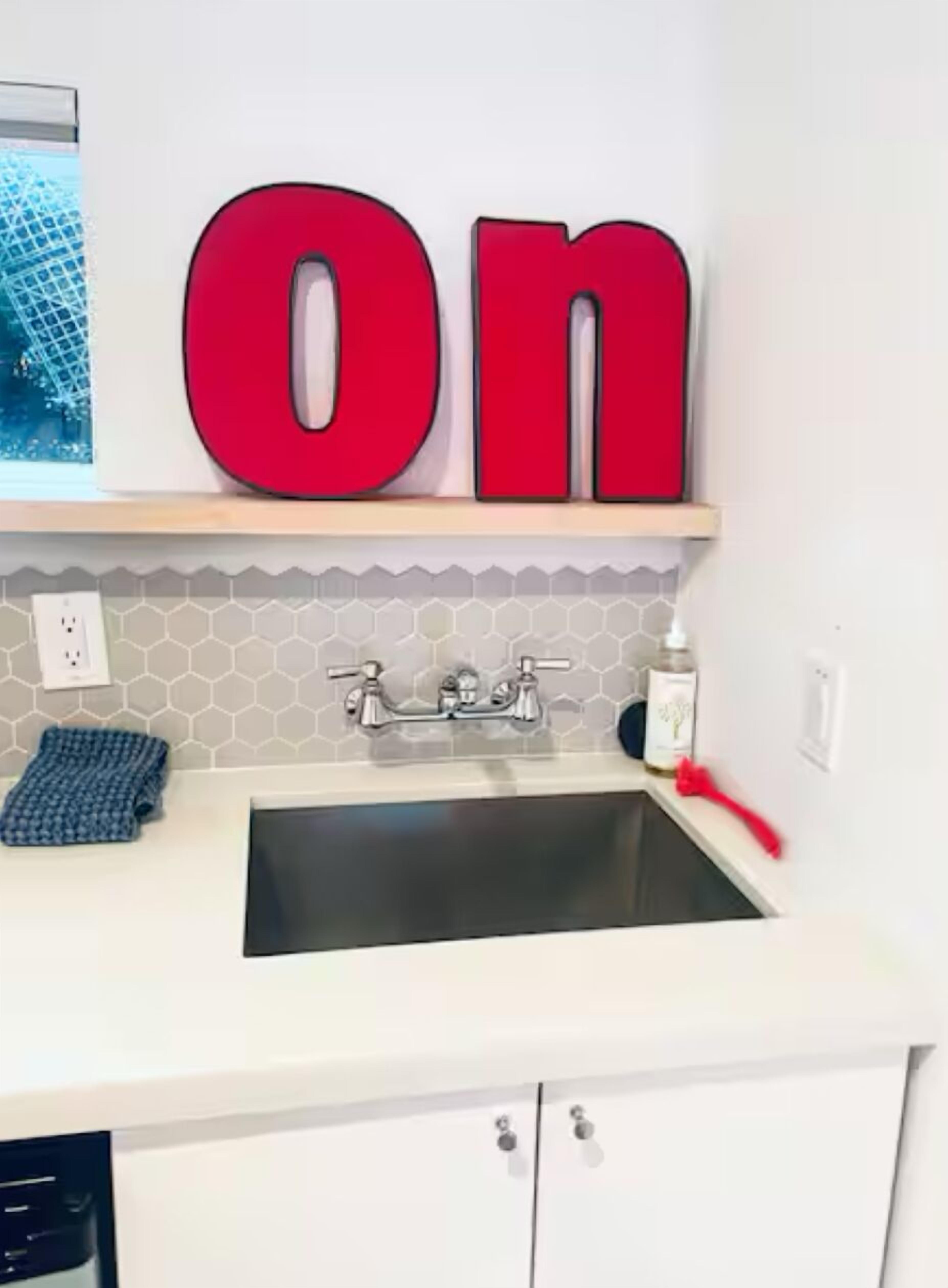 A kitchen with a white countertop, a stainless steel sink, and a red 'ON' sign above it.