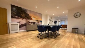 Un espace repas moderne avec un plancher en bois, un grand tableau représentant une scène de plage et une table à manger avec des chaises.