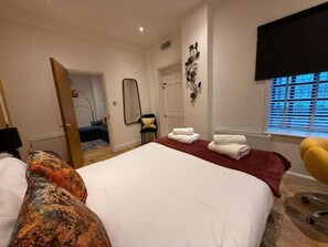 Ein Hotelzimmer mit einem großen Bett, einem Sessel, einem Spiegel und einem Fenster mit Jalousien.