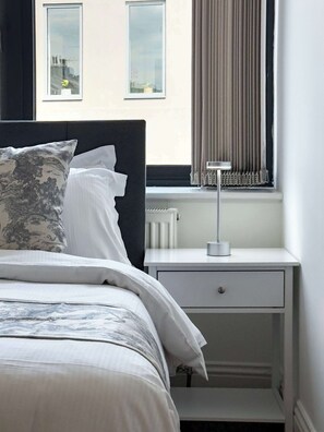 A bedroom with a bed, a bedside table with a lamp, and a window with curtains.