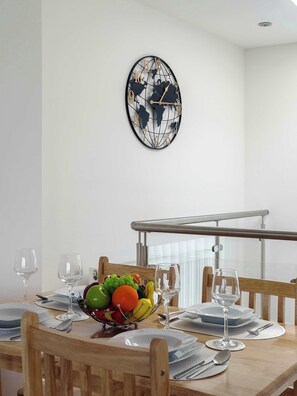 A dining area with a round table set for four, a fruit bowl, and a wall clock with a world map design.