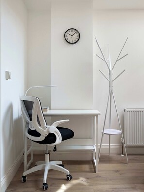 Un espace de bureau moderne comprenant un bureau blanc, une chaise blanche à roulettes, un porte-manteau et une horloge murale.