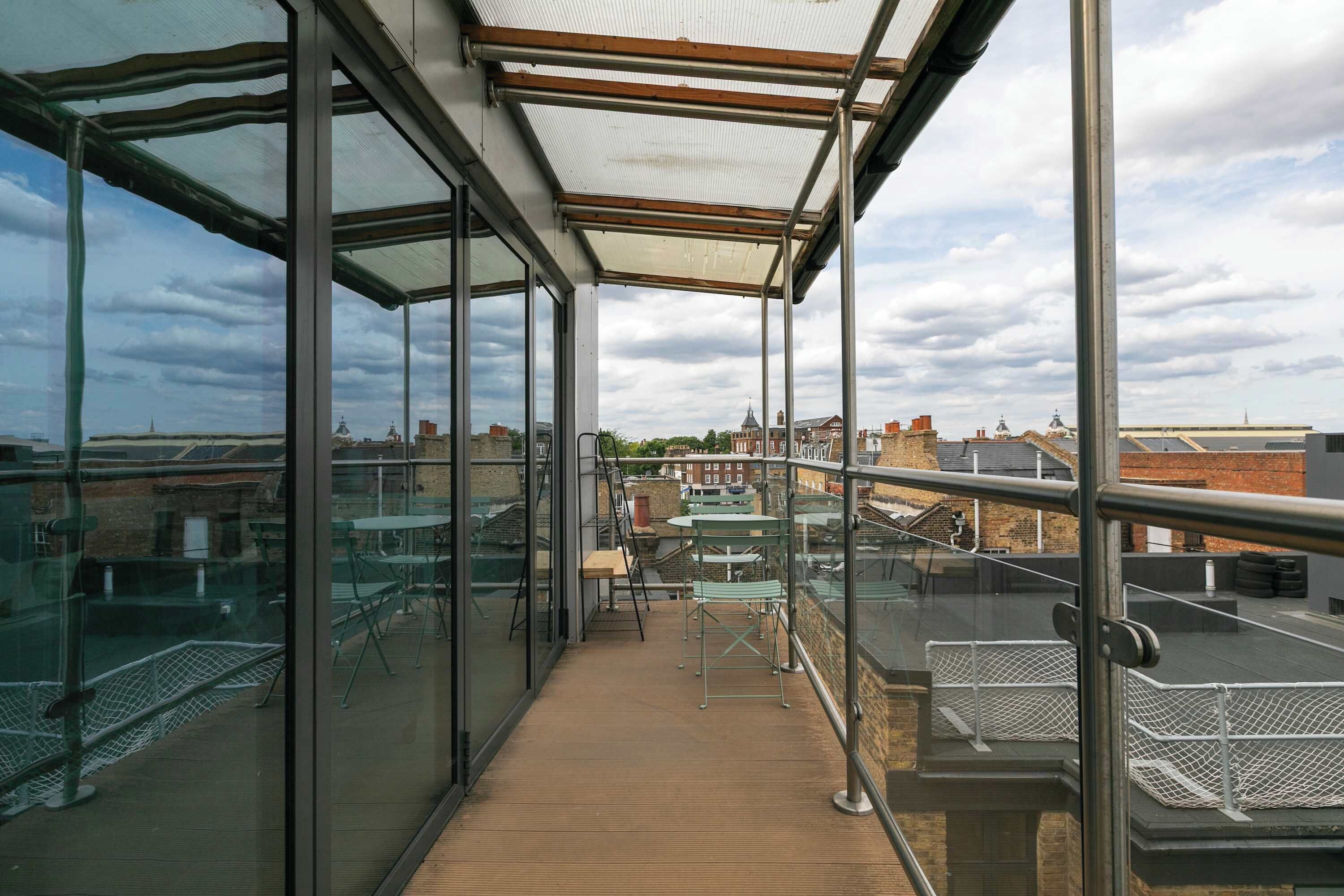 A glass-enclosed balcony with a wooden floor, metal railings, and a view of the cityscape.