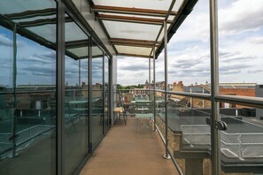 A glass-enclosed balcony with a wooden floor, metal railings, and a view of the cityscape.
