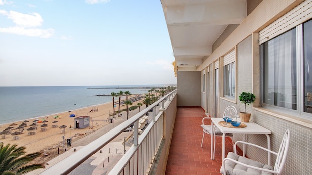 Un balcón con vista a la playa, una mesa con sillas y una planta en maceta.