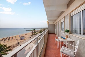 Un balcón con vista a la playa, una mesa con sillas y una planta en maceta.