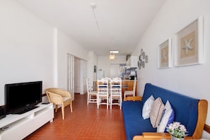 Una sala de estar con televisor, sofá, mesa de comedor, sillas y una cocina al fondo.