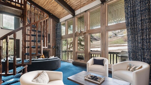 A spacious living area with a wooden staircase, comfortable seating, and large windows offering a view of the outdoors. - 3BR Penthouse, Hot Tub, Mtn Views! Hiking Trails! (Snowmass Village)