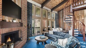 A spacious living room with a fireplace, a curved staircase, and a large window. - 3BR Penthouse, Hot Tub, Mtn Views! Hiking Trails! (Snowmass Village)