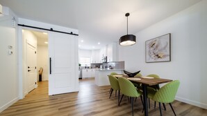 A modern kitchen with white cabinets, a central island, and a dining area with green chairs.