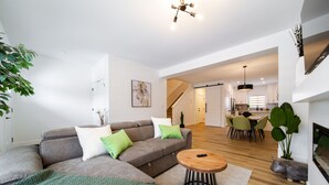 A modern living room with a grey sofa, green and white cushions, a wooden coffee table, and a staircase leading to a kitchen area.