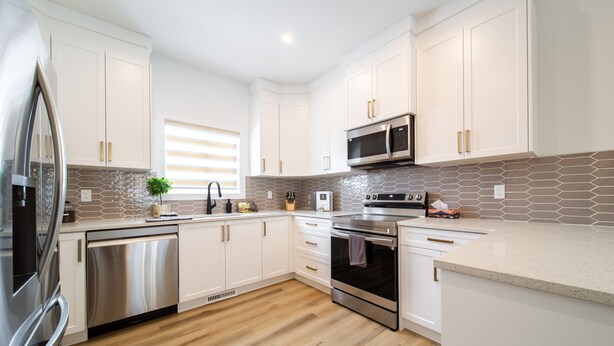 A modern kitchen with white cabinets, stainless steel appliances, and a herringbone tile backsplash.