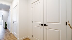 A hallway with white doors, a wooden floor, and a potted plant.