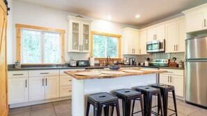 A modern kitchen with white cabinets, a central island with stools, a microwave, a refrigerator, and a window with a view of trees. - Artist's farm house children loft m/s Redmond, Seattle (Duvall)