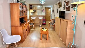 A compact living space with a kitchen area, wooden furniture, a dining table, and a TV.