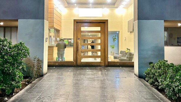 A hotel entrance with a modern design, featuring a glass door, a reception desk, and a seating area visible through the door.