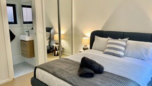 A modern bedroom with a bed, bedside lamps, a mirror, and a bathroom with a sink and towel rack.